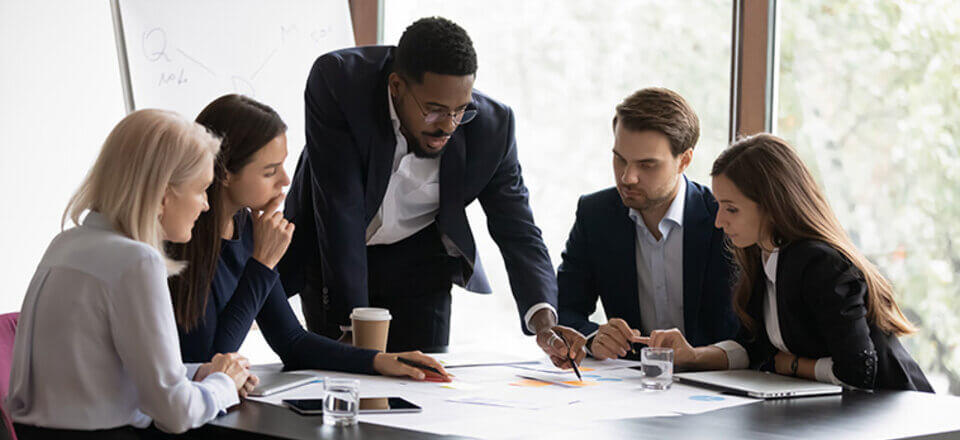 People leaning over a table in a sunny conference room, looking at a print out together.